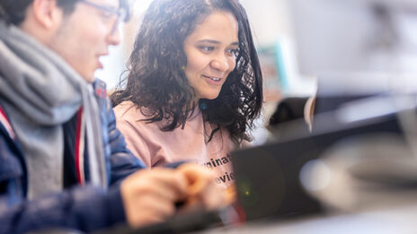 Foto von einer Schüler und einem Schüler, die in einen Laptop schauen.