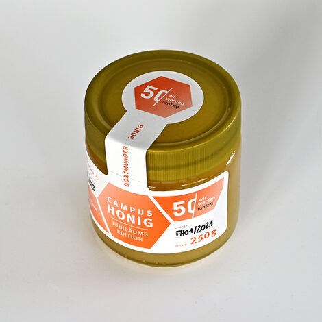 Produktaufnahmen eines Honigglases im Look des Jubiläums-Etikett. Auf dem Etikett seht "Campus Honig - Jubiläums Edition" und es zeigt das Logo 50 Jahre Fachhochschule Dortmund.