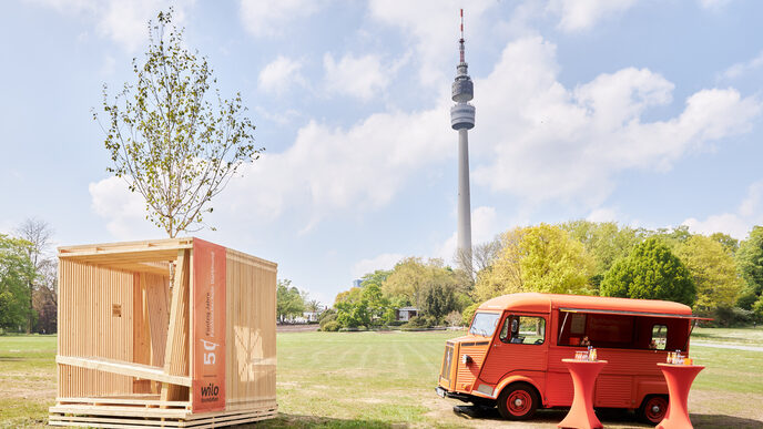 A wooden construction in the shape of a cube stands on a meadow.