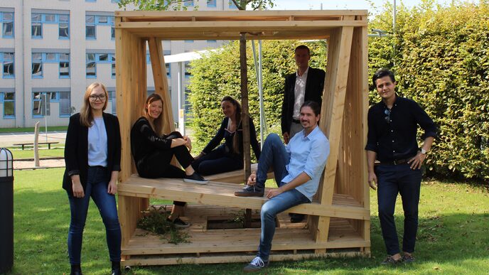 Eine Gruppen von Menschen sitzt auf einer Holzkonstruktion am Campus der FH Dortmund.