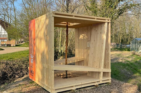 A wooden construction in the shape of a cube stands on a meadow.