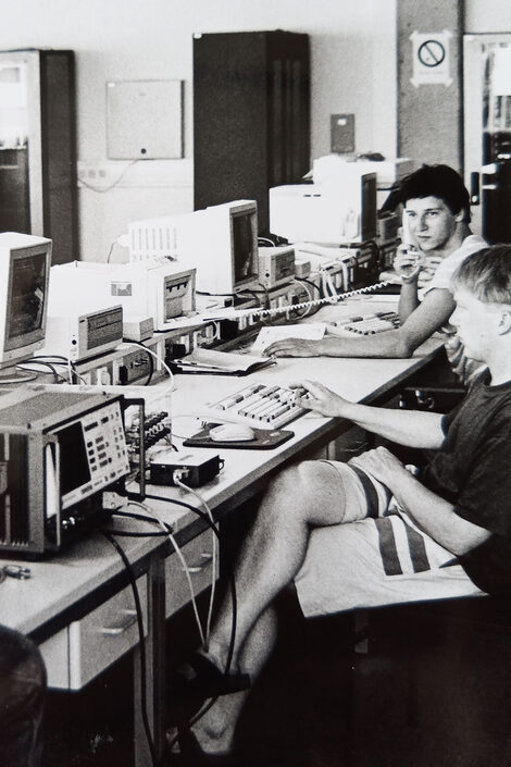 Zwei Studierende sitzen vor elektronischen Geräten im Fachbereiche Telekommunikationsbild. Das Bild ist schwarz-weiß, die Technik sieht für heutige Maßstäbe alt und urig aus.