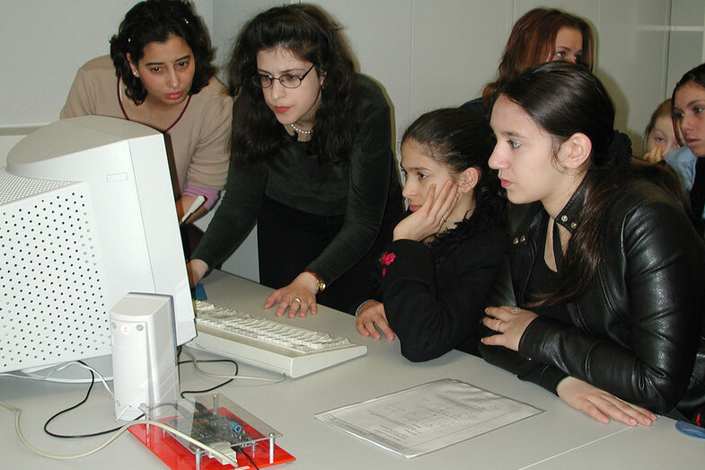 Several young women look at a CRT monitor.