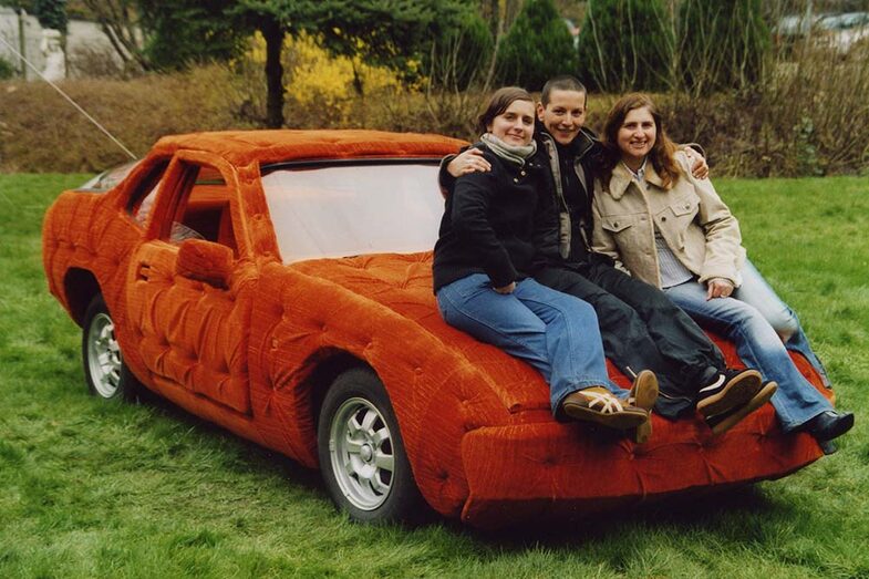 Three women sit on a car that is completely covered in plush.