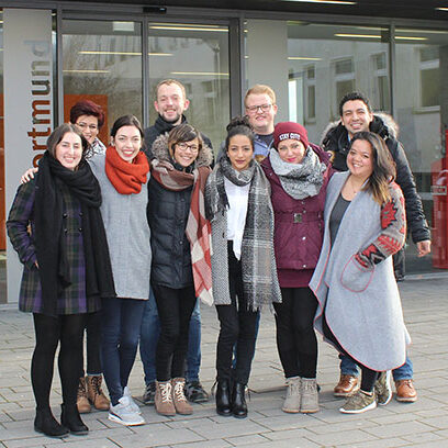 Eine Gruppe junger Erwachsener steht vor einem Gebäude der FH Dortmund.