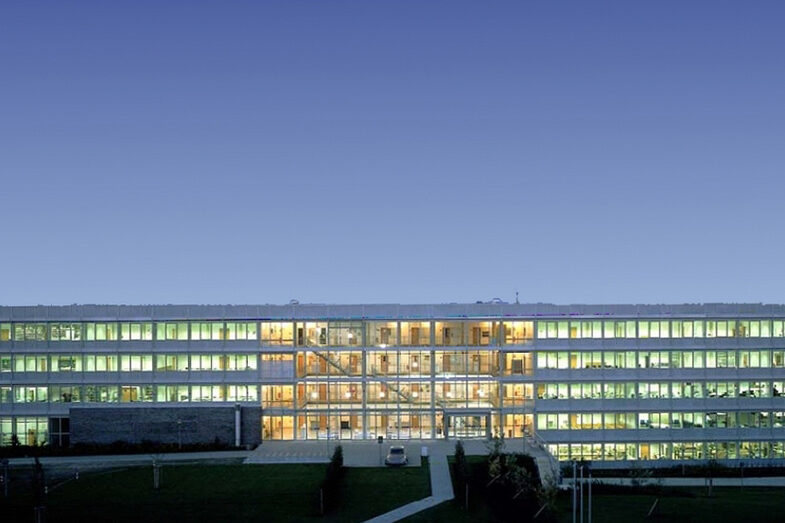 Bild des Gebäudes Emil-Figge-Straße 40 in der Abenddämmerung. Die meisten Fenster der langen Glasfassade sind erleuchtet.