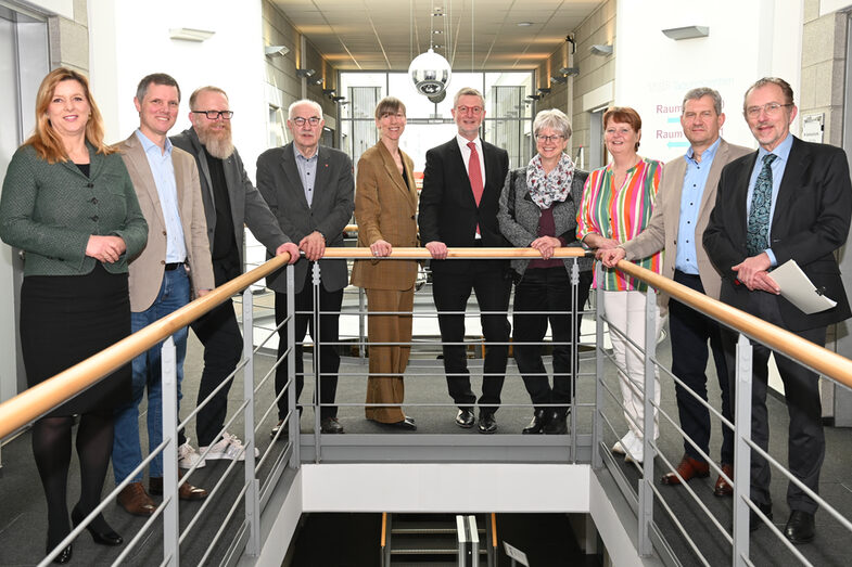 Ten people stand behind a U-shaped railing and look into the camera.