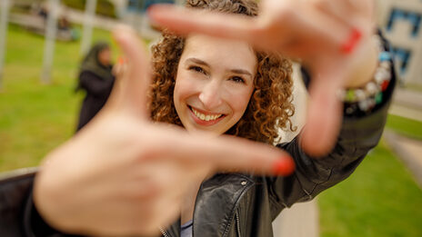 Photo of a student forming a square with her index fingers and thumb in front of her and looking through it.