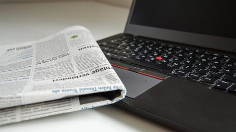 Foto einer zusammengefalteten Zeitung, die auf der Tastatur eines Laptops liegt.