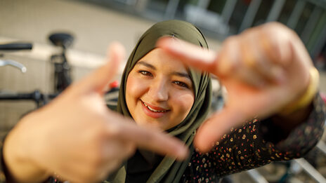 Photo of a student forming a square with her index fingers and thumb in front of her and looking through it.