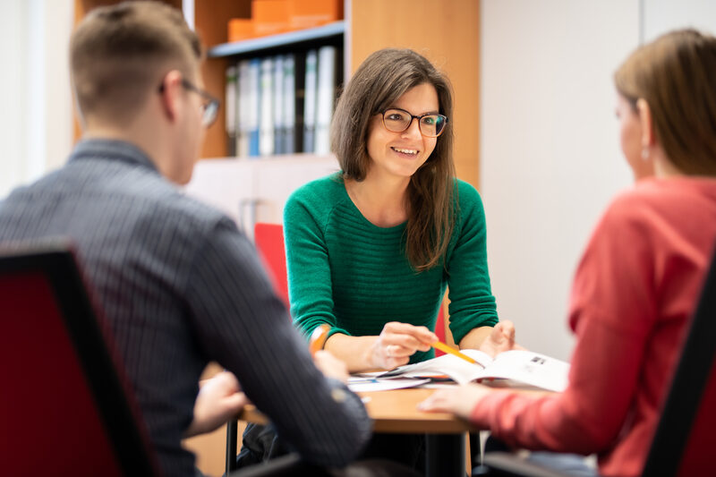 Photo of an employee advising a student at a table. She is holding a ballpoint pen and documents.