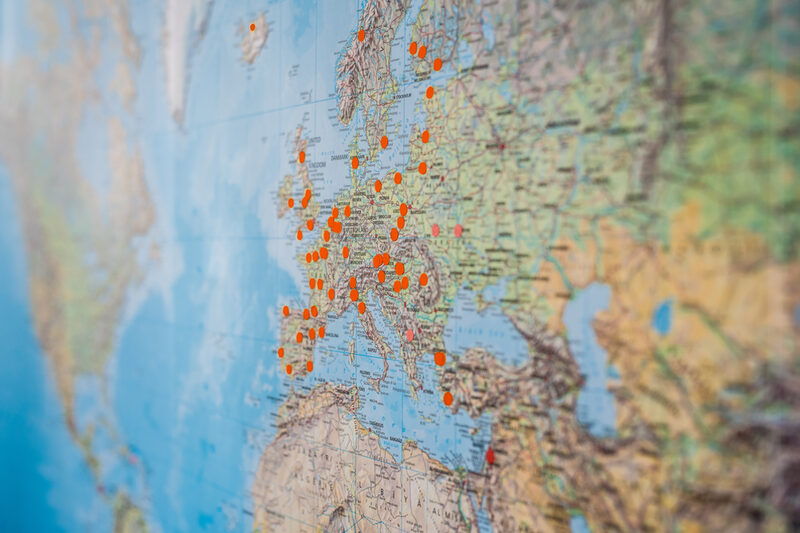 Nahaufnahme einer Weltkarte, auf der mit orangenen Punkten Orte markiert sind.