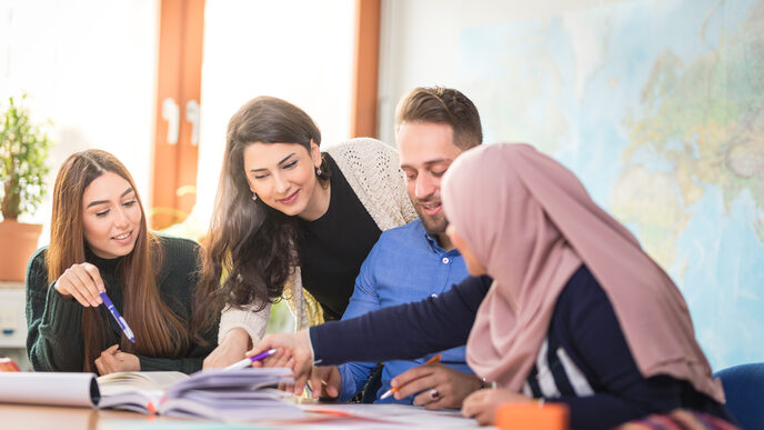 Foto von vier internationalen Studierenden, die gemeinsam Unterlagen diskutieren, die vor ihnen auf einem Tisch liegen.