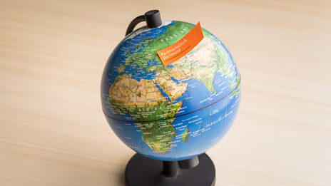 Photo of a globe with a note with the FH word mark stuck to it.