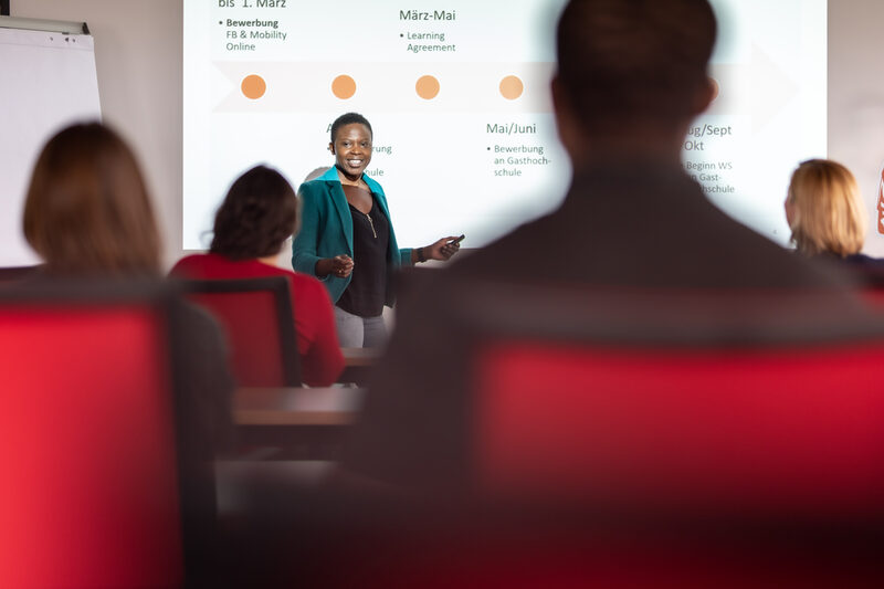 Photo of an information event organized by the International Office in a lecture hall. A lecturer is standing in front of a projected slide.