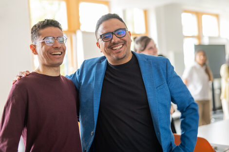 Zwei internationale Studenten legen lachend den Arm umeinander.