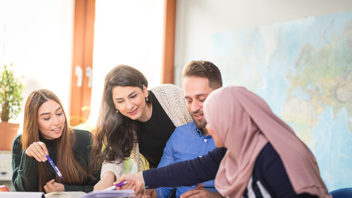 Foto von vier internationalen Studierenden, die gemeinsam Unterlagen diskutieren, die vor ihnen auf einem Tisch liegen.