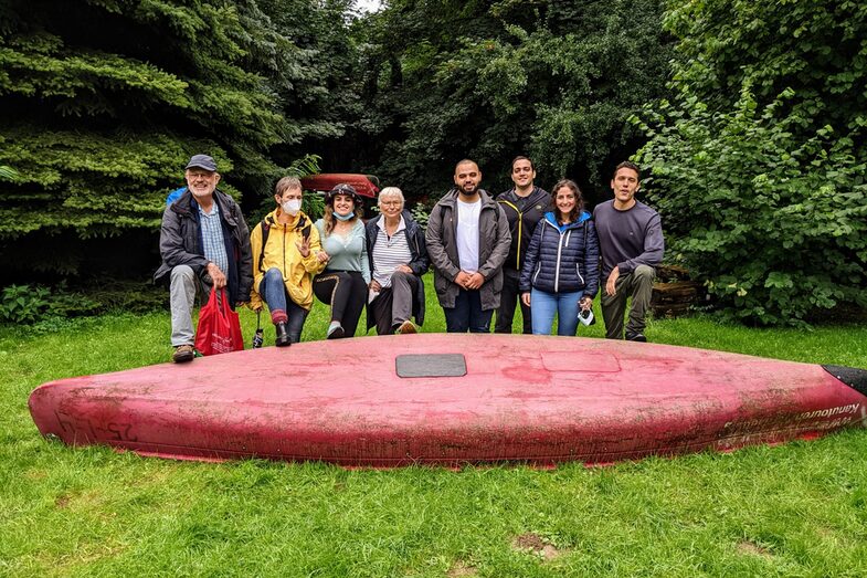 TeilnehmerInnen des Seniorenpatenschaftsprogramms beim Ende einer Kanutour. Das Kanu liegt vor ihnen. Dahinter stehen 3 SeniorInnen und 5 internationale Studierende__Participants of the senior mentoring program at the end of a canoe trip. The canoe lies in front of them. Behind it there are 3 senior students and 5 international students.