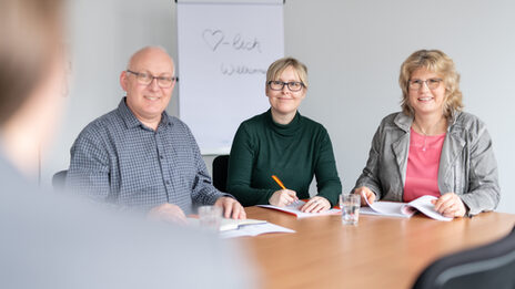 Photo of a job interview situation with 3 HR employees sitting next to each other at a table. An applicant is sitting across from them - very blurred and cropped in the picture. __ <br>Job interview situation with 3 employees of the HR department who are sitting next to each other at the table. An applicant is sitting across from you - in the picture very blurred and in a bleed.