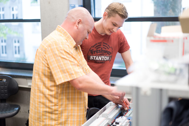 Photo of an employee working on an appliance while an apprentice looks over his shoulder.