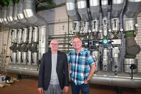 Two people in a room with many large pipes on the back wall.