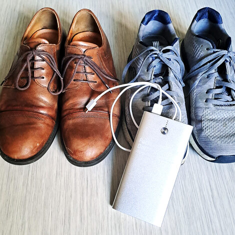 Two pairs of shoes stand next to each other on the floor. A power bank lies in front.