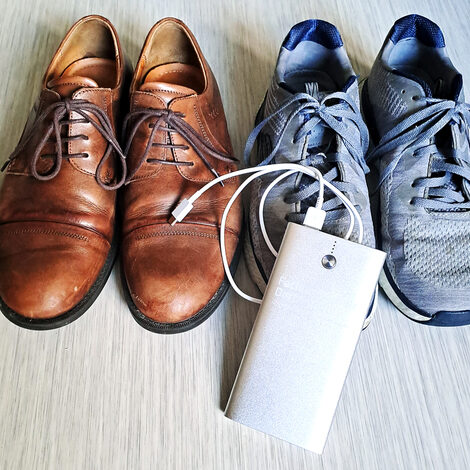 Zwei Paar Schuhe stehen nebeneinander auf dem Boden. Vorn liegt eine Powerbank.