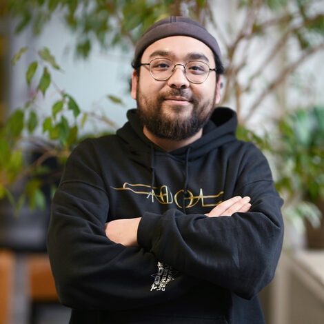 A person in a black hoodie looks into the camera with a smile.