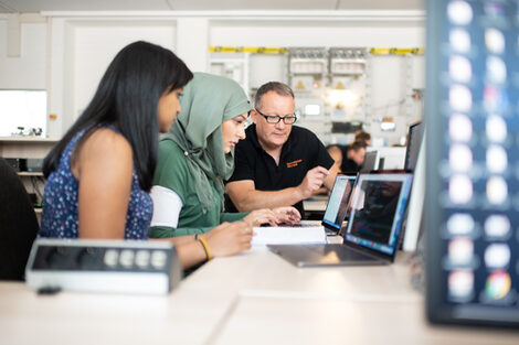 Photo of two students and a professor in the laboratory for energy automation and grid management. They are sitting next to each other and looking at a laptop screen together.