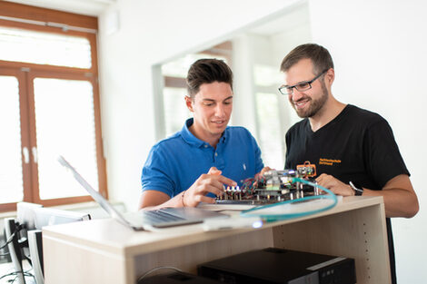 Photo of a student and an employee of the Laboratory for Energy Automation and Grid Management. They are standing next to each other and working on an electronic test setup.