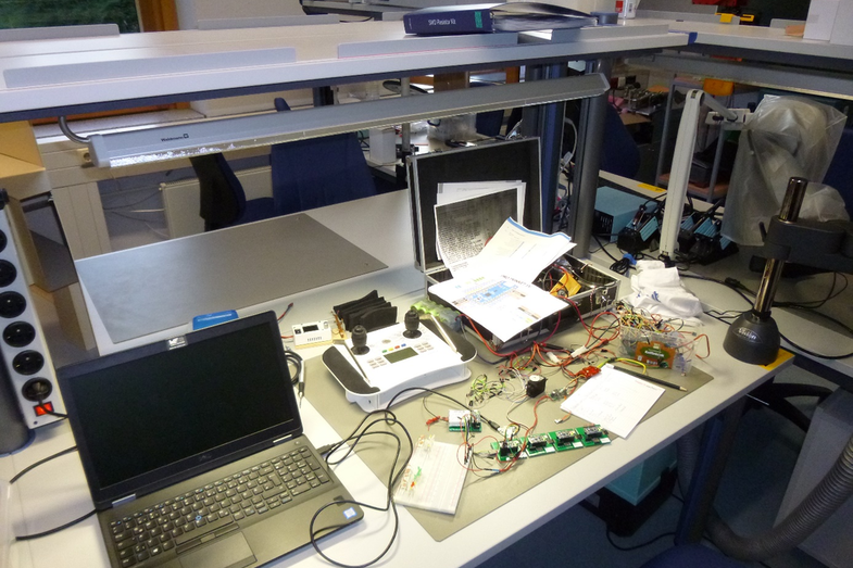 Photo of a table with a laptop, lots of cables and various technical devices, such as a digital remote control.