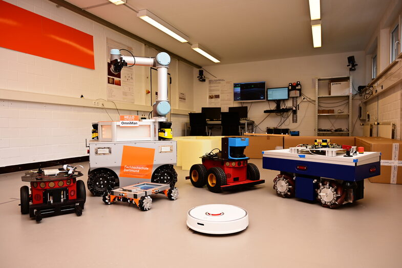 Anordnung von sechs mobilen Robotern mit Arbeitsplatz im Roboter-Labor__Arrangement of six mobile robots with a workstation in the robotics lab.