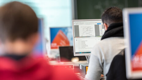 Foto von zwei Studierenden in Rückansicht in PCs in einem Computerraum.