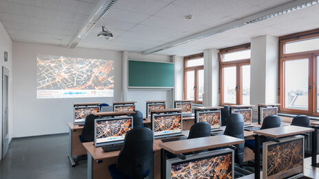 Room shot of a laboratory in the Faculty of Information Technology with rows of seats and PCs. Something is beamed onto the wall of the room.