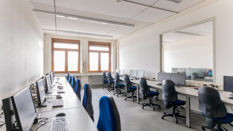 Room shot of a laboratory with tables and computer workstations, lined up on the right and left of the wall.