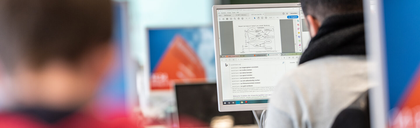 Photo of two students in rear view in PCs in a computer room.