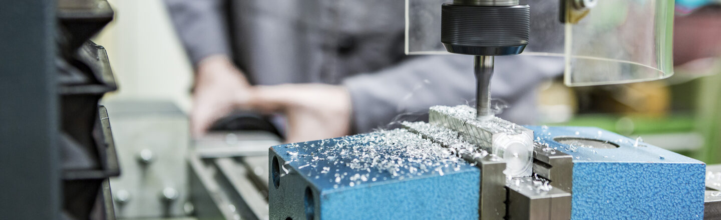 Foto einer Person, die mit einer Fräsmaschine in der mechanischen Werkstatt arbeitet. Die Maschine fräst etwas in ein Stück Metall.