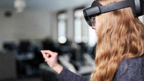 Foto von einer Person, die eine VR-Brille trägt. Sie greift mit der rechten Hand vor sich.
