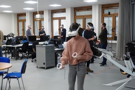 Studierende in der Lehrveranstaltung Extended Realty tragen Virtual Reality-Headsets und interagieren mit einer virtuellen Szene.__Students in the Extended Reality course wear virtual reality headsets and interact with a virtual scene.