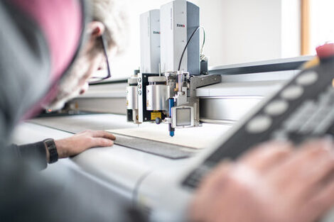 Foto von einem Mann, der am Laser-Cutter arbeitet und eine Platte zurecht schneidet.