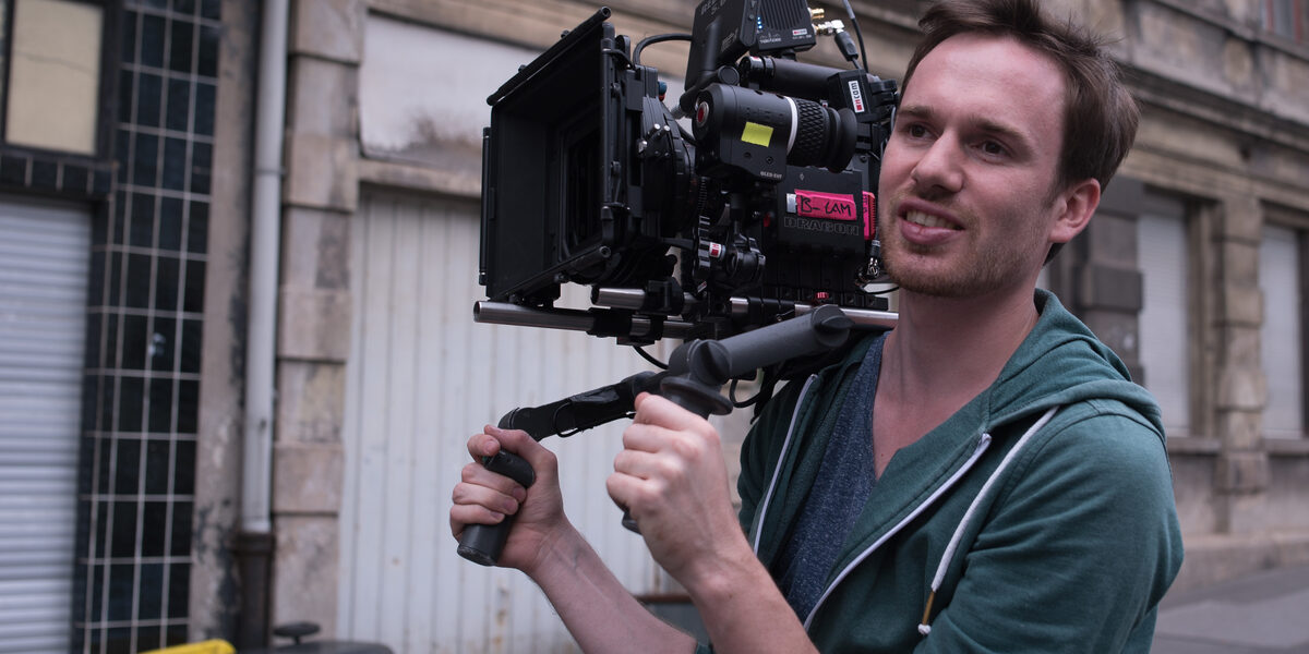 Portrait of Tobias Lohf, carrying a camera on his shoulder.