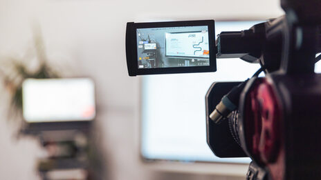 Photo of a video camera with an opened display through which you can see the setup of the laptop and digital whiteboard.