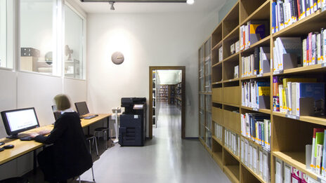 Photo of a room in the library featuring a book shelf, a multi-purpose device for photocopying, printing and scanning, and several computer desks__Photo of a room in the library featuring a book shelf, a multi-purpose device for photocopying, printing and scanning, and several computer desks