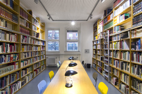 Foto des Lesesaals in der Bibliothek mit Bücherregalen, Tischen, Leselampen und Stühlen__Photo of the library reading room with book shelves, desks, reading lamps and chairs