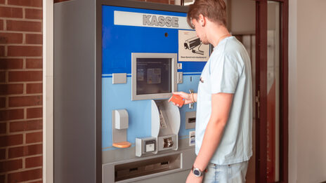 Foto von einem jungen Mann, der den Kassenautomaten vor der Bibliothek bedient.