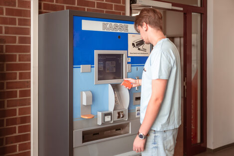 Foto von einem jungen Mann, der den Kassenautomaten vor der Bibliothek bedient.