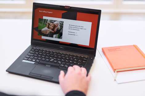 Foto eines Laptops, auf dem die Folie einer Präsentation mit der Überschrift „Noch offene Fragen?“ aufgerufen ist. Die Hand einer Person liegt auf der Tastatur.