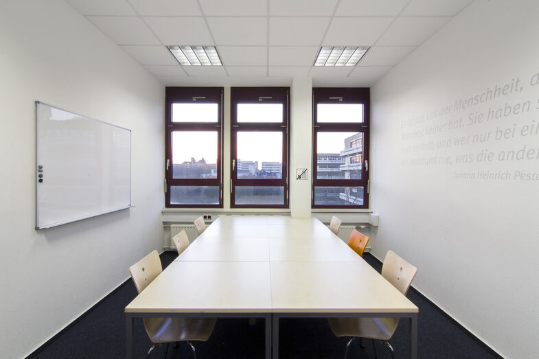 Foto eines Gruppenarbeitsraums in der Bibliothek mit Tischen und Stühlen für sechs Personen__Photo of a group study room in the library, equipped with desks and chairs for six people