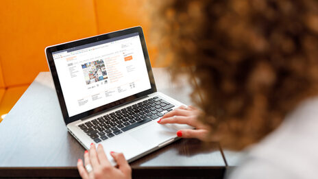 Foto über die Schulter einer Studentin auf einen Laptop, auf dem die Website der Fachhochschule Dortmund aufgerufen ist.__A femal student is sitting and visiting the website of Fachhochschule Dortmund on her laptop.