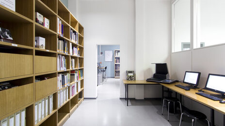 Photo of a room in the library featuring a book shelf, a scanner and several computer desks__Photo of a room in the library featuring a book shelf, a scanner and several computer desks